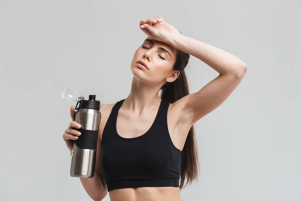 Mooie jonge sport fitness vrouw drinkwater geïsoleerd over grijze muur achtergrond. — Stockfoto