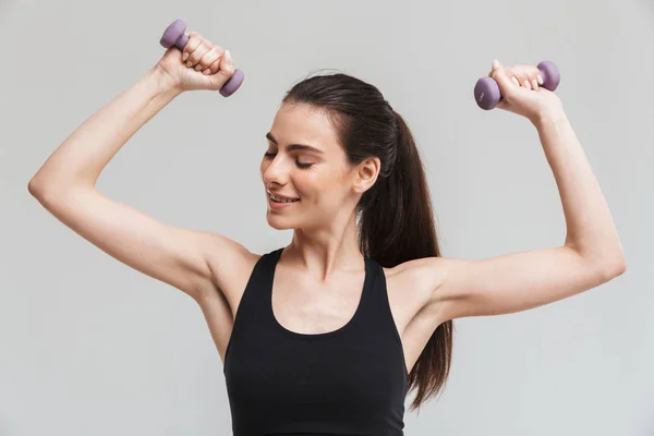 Sport fitness vrouw maken oefeningen met dumbbells geïsoleerd over grijze muur achtergrond. — Stockfoto