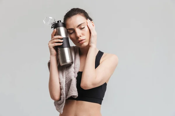 Schöne junge müde Sport Fitness Frau posiert mit Handtuch und Flasche mit Wasser isoliert über graue Wand Hintergrund. — Stockfoto