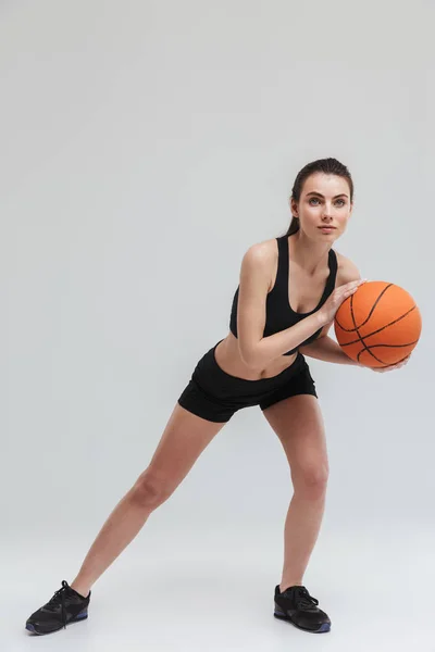 Młody Sport fitness kobieta gracz zrobić ćwiczenia grać koszykówki na białym tle na szarym ścianie. — Zdjęcie stockowe