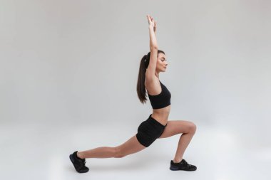 Güzel genç spor fitness kadın gri duvar arka plan üzerinde izole egzersizleri yapmak.