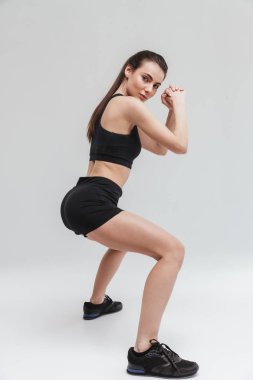 Güzel genç spor fitness kadın gri duvar arka plan üzerinde izole egzersizleri yapmak.