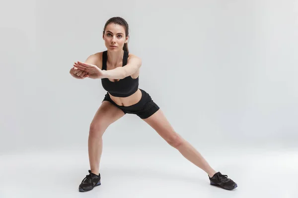 Mooie jonge sport fitness vrouw maken oefeningen geïsoleerd over grijze muur achtergrond. — Stockfoto