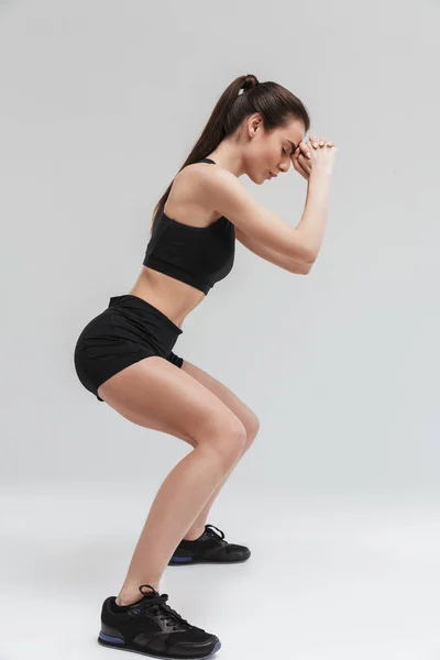 Krásná mladá sportovní fitness žena provádí cvičení izolovaná na pozadí šedé zdi. — Stock fotografie