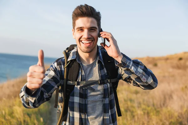 Happy young man outside in free alternative vacation camping talking by mobile phone.