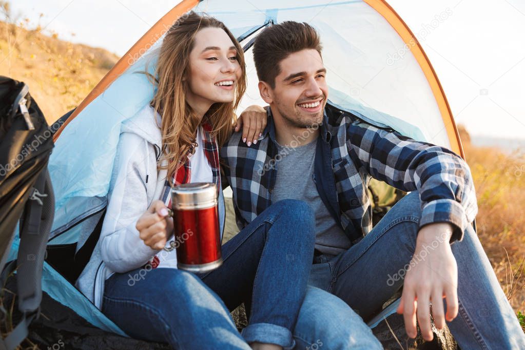 Happy young loving couple outside in free alternative vacation camping drinking hot tea.