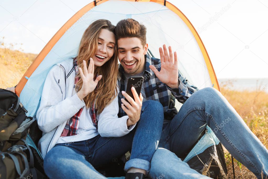 Happy young loving couple outside in free alternative vacation camping talking by mobile phone.