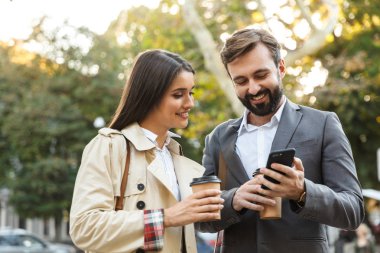 Başarılı ofis çalışanları adam ve kadın şehir caddesinde cep telefonu kullanırken paket kahve tutan Fotoğraf