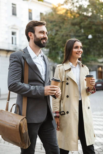 Photo of joyful office workers man and woman in formal wear drinking takeaway coffee while walking on city street — Stock Photo, Image