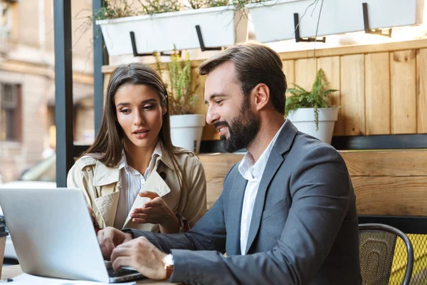 Portrait of caucasian business couple man and woman having conversation and working on laptop together while sitting in cafe outdoors — Stock Photo, Image