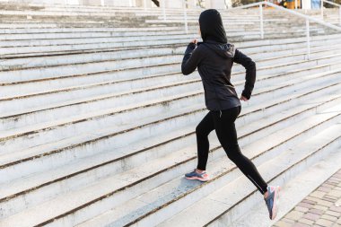 Genç müslüman spor fitness kadın hijab ve sokakta açık havada çalışan koyu giysiler giymiş.