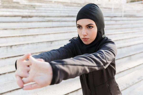 Мусульманские серьезные спортивные фитнес-женщина одета в хиджаб позирование сделать спорт растяжения упражнения на улице с шагами на заднем плане . — стоковое фото
