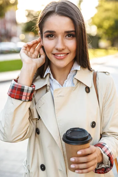 Şehir caddesinde yürürken iyimser sevimli kadın paket kahve içme ve kamera gülümseyen Portresi — Stok fotoğraf