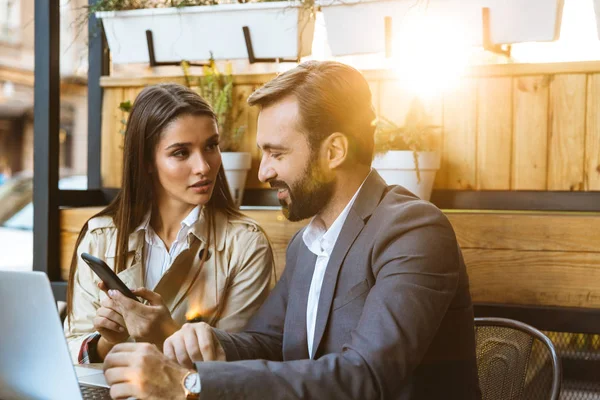 Portrait of professional business couple man and woman having conversation and working on laptop together while sitting in cafe outdoors — Stock Photo, Image