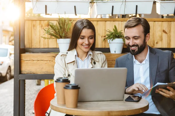 Retrato de pareja de negocios satisfechos hombre y mujer conversando y trabajando juntos en el portátil mientras están sentados en la cafetería al aire libre — Foto de Stock