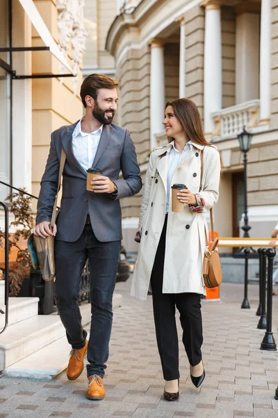 Portrait of elegant business couple man and woman drinking takeaway coffee and talking together while walking through city street — Stock Photo, Image