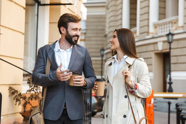 Porträt eines jungen Geschäftsmannes und einer Frau, die Kaffee zum Mitnehmen trinken und miteinander reden, während sie durch die Straßen der Stadt laufen — Stockfoto