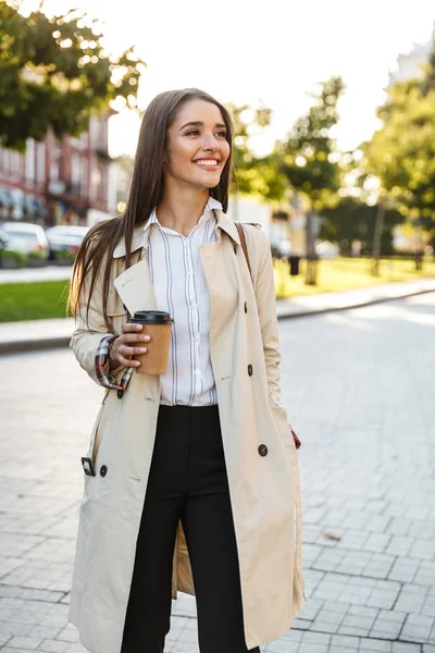 Retrato de la alegre mujer caucásica tomando café para llevar y sonriendo a un lado mientras camina por la calle de la ciudad —  Fotos de Stock