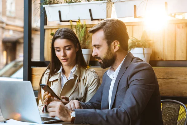 Portrait of successful business couple man and woman having conversation and working on laptop together while sitting in cafe outdoors — Stock Photo, Image