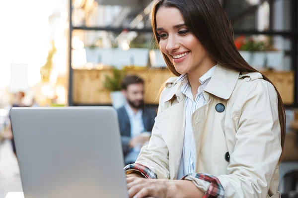 Πορτρέτο της χαρούμενη νεαρή επιχειρηματίας φορούν χαμογελαστά και δουλεύοντας σε φορητό υπολογιστή, ενώ κάθονται στο καφέ σε εξωτερικούς χώρους — Φωτογραφία Αρχείου