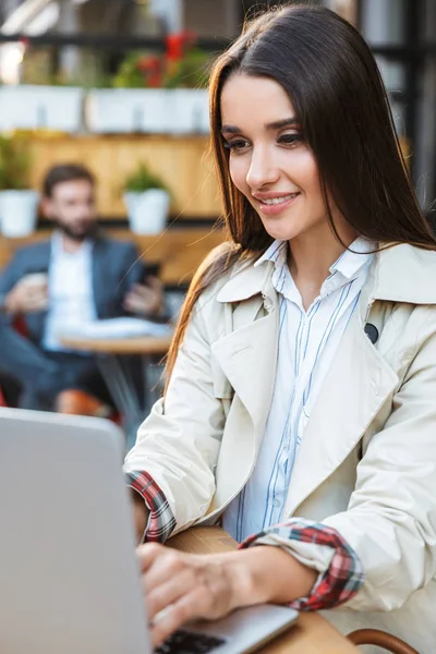 Πορτρέτο της όμορφης νεαρής επιχειρηματία χαμογελώντας και δουλεύοντας στο φορητό υπολογιστή, ενώ κάθονται στο καφέ σε εξωτερικούς χώρους — Φωτογραφία Αρχείου