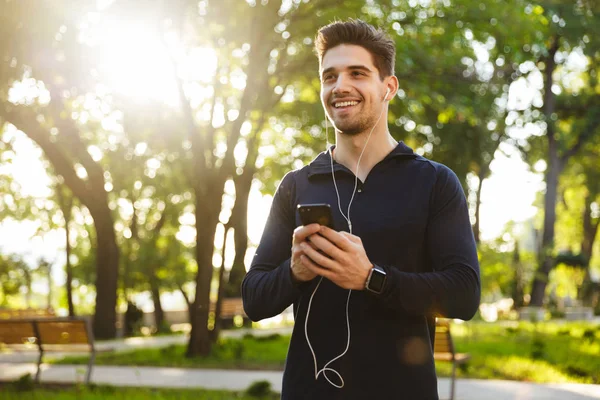 Wesoły optymistyczny młody Sport fitness człowiek stojący w zielonym parku przyrody za pomocą telefonu komórkowego rozmowy — Zdjęcie stockowe