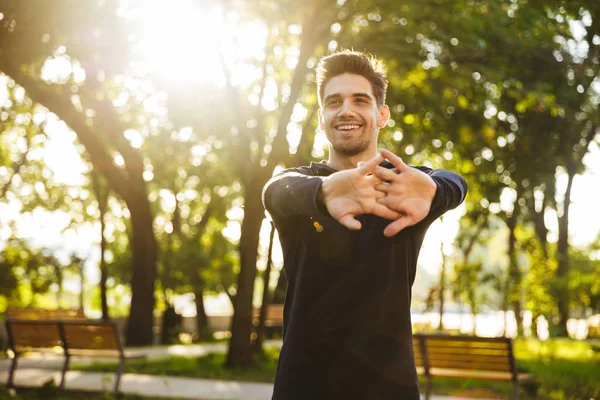 Vidám fiatal sport fitness ember állt a zöld Park jellege, hogy Stretching gyakorlatok fegyverek. — Stock Fotó