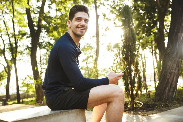 Porträt eines zufriedenen, athletischen Mannes, der auf der Bank sitzt und die Arme in der Hand hält — Stockfoto