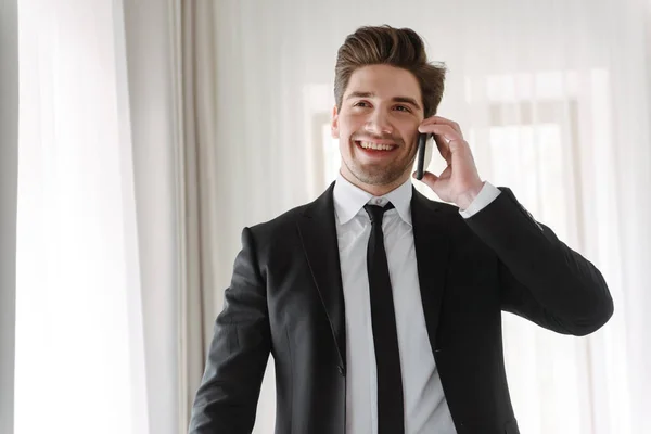 Gülümseyen yakışıklı işadamının otel dairesinde cep telefonuyla konuşurken çekilmiş fotoğrafı — Stok fotoğraf