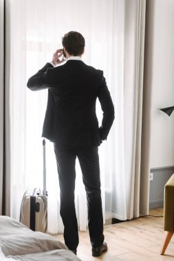 Otel dairesinde bagaj ile cep telefonu konuşurken esmer işadamı düşünme Fotoğrafı