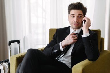 Otel dairesinde koltukta otururken cep telefonu yla konuşan sakinleştirici esmer işadamının fotoğrafı