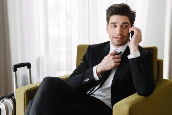 Φωτογραφία του κατευναστικό μελαχρινή επιχειρηματίας μιλάει στο κινητό τηλέφωνο, ενώ κάθεται στην πολυθρόνα στο ξενοδοχείο διαμέρισμα — Φωτογραφία Αρχείου