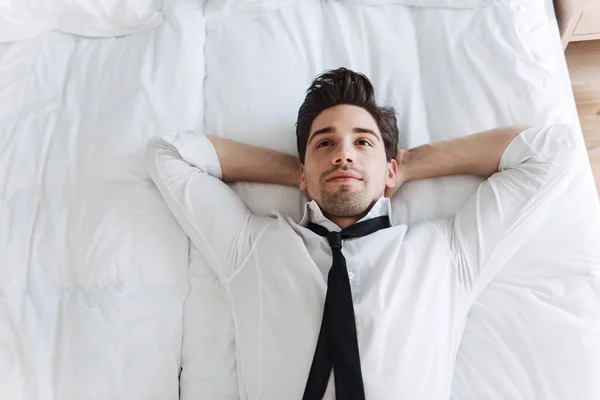 Photo from top of european calming businessman lying on bed in hotel apartment — Stock Photo, Image