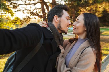 Park doğasında açık havada yürüyüş poz mutlu genç güzel sevgi dolu çift kamera ile selfie çekmek.