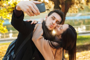 Park doğasında açık havada yürüyüş poz güzel seven çift cep telefonu ile selfie çekmek.