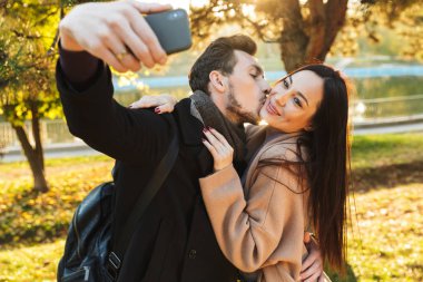 Park doğasında açık havada yürüyüş poz güzel seven çift cep telefonu ile selfie çekmek.