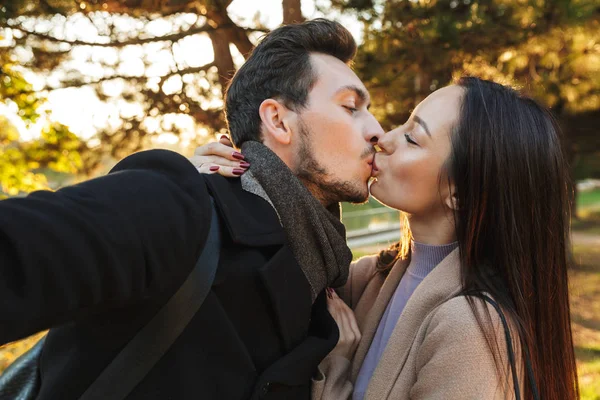 Feliz joven hermosa amante pareja posando caminando al aire libre en parque naturaleza tomar selfie por cámara besos . —  Fotos de Stock