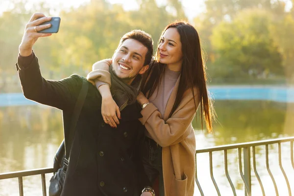 Jovens felizes belo casal amoroso posando andando ao ar livre no parque natureza tirar selfie por telefone móvel . — Fotografia de Stock