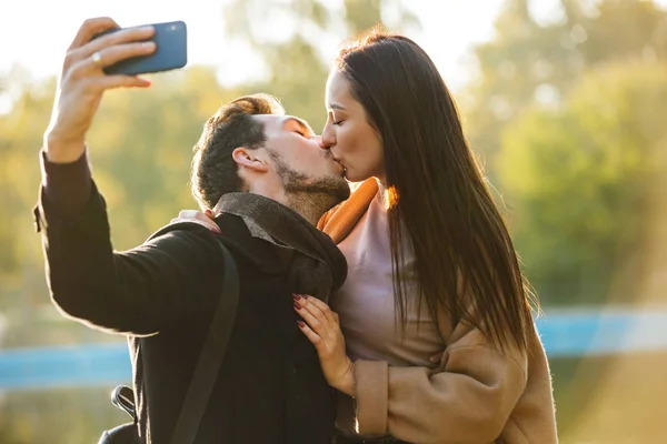 Jovens felizes belo casal amoroso posando andando ao ar livre no parque natureza tirar selfie por telefone celular beijando . — Fotografia de Stock