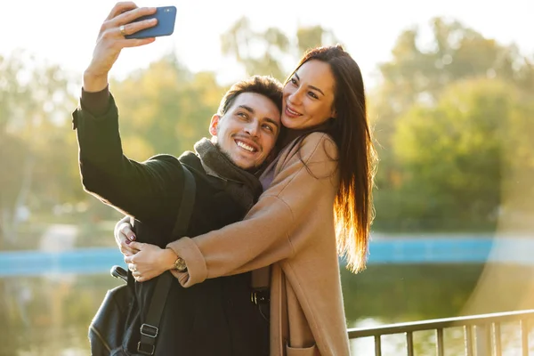 Jovens felizes belo casal amoroso posando andando ao ar livre no parque natureza tirar selfie por telefone móvel . — Fotografia de Stock