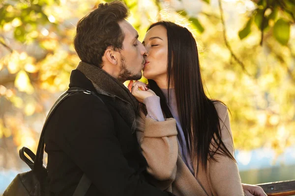 Glückliche junge schöne liebende Paar posiert zu Fuß im Freien im Park Natur auf Bank sitzend. — Stockfoto