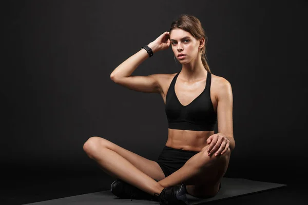 Retrato de mujer caucásica concentrada en ropa deportiva sentada y descansando en caja de hormigón después del entrenamiento en el gimnasio —  Fotos de Stock