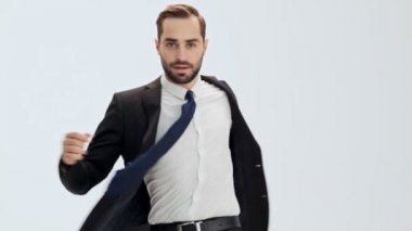 Siyah takım elbiseli ve mavi kravatlı ciddi genç işadamı kameraya dönerek ceketini gri arka plan üzerinde ilikleyerek izole