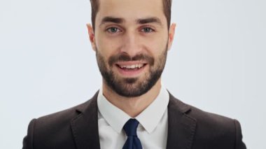 Siyah takım elbise ve mavi kravat ile çekici genç işadamının kırpılmış görünümü, izole gri arka plan üzerinden kameraya bakarken gülümseyen