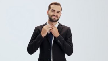 Siyah takım elbiseli ve mavi kravatlı yorgun genç işadamı ceketinin düğmelerini çözüp, gri arka plan izole üzerinden kameraya bakarken kravatını çıkarıyor