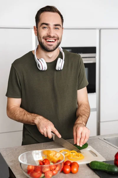 Šťastný mladý fešák pózný v kuchyni doma a poslouchá hudbu se sluchátky. — Stock fotografie