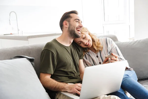 Feliz emocionado joven pareja amorosa sentada en el sofá en casa utilizando el ordenador portátil . — Foto de Stock