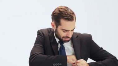 Siyah takım elbiseli ve mavi kravatlı neşeli genç işadamı akıllı telefonlarını iç cebinden çıkarıp gri arka plan üzerinden izole bir çağrı yapıyor.