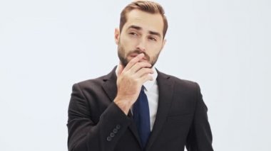 Siyah takım elbise li ve mavi kravatlı pensive genç işadamı bir şey hakkında düşünme ve gri arka plan izole üzerinde kameraya bakarken çenesini dokunmadan