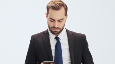 Siyah takım elbiseli ve mavi kravatlı genç işadamı akıllı telefonlarını iç cebinden çıkarıp, gri arka plan izole üzerinde konuşmak istemediği birinden telefon alıyor.